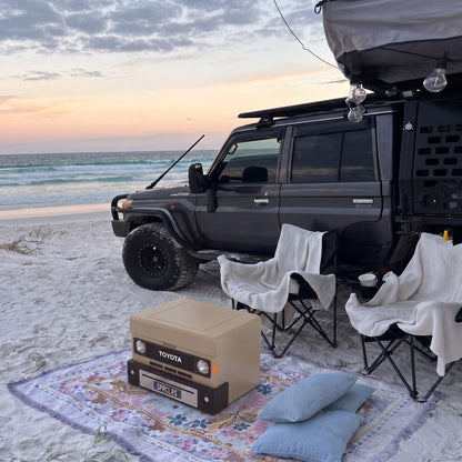 Sandy Taupe ute mini cooler on a beach rug in front of camp chairs and a 70 Series